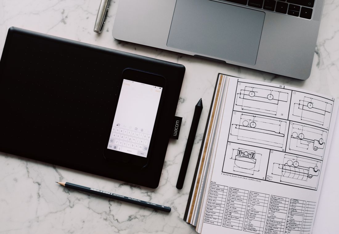 Overhead view of a design desk with laptop, tablet and technical sketches